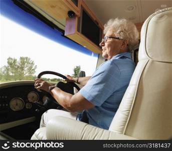Senior adult woman driving RV and smiling.