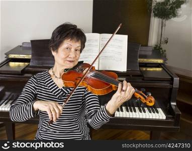 Senior adult woman playing the violin at home with piano in background