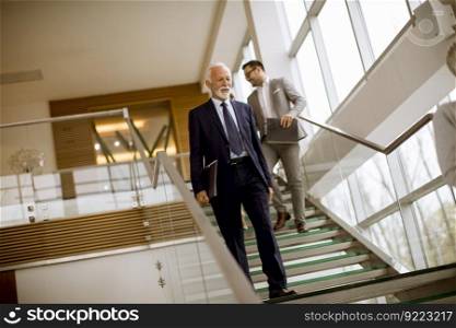 Senior and young busenessmen coming down the stairs in office