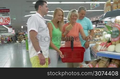 Senior and young couples standing at the showcase with cheese and choosing the sort they want. Shopping for food in the supermarket