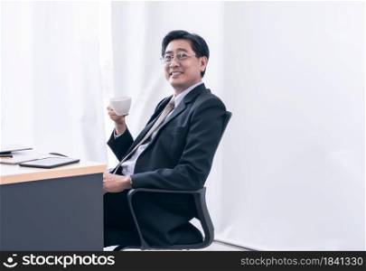 Senior asian business man is happily smiling and drinking coffee in workplace