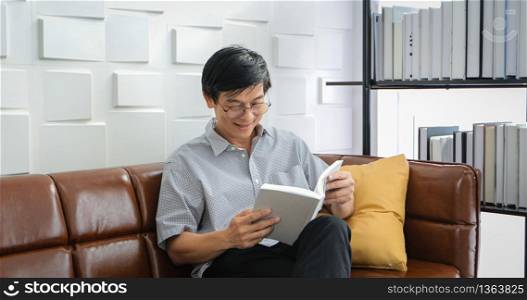 Senior Asian man reading book on sofa in living room at home ,Portrait of Asian elderly man is Relaxing and Happiness With Read a Magazine