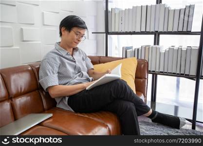 Senior Asian man reading book on sofa in living room at home ,Portrait of Asian elderly man is Relaxing and Happiness With Read a Magazine