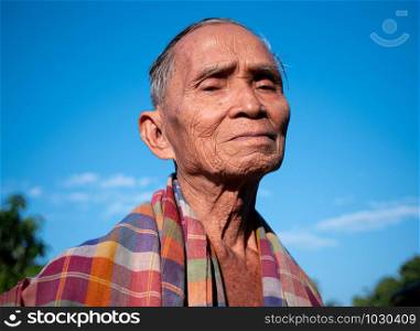 Senior Asian man with a loincloth covering his shoulders, standing over the bright sky background.