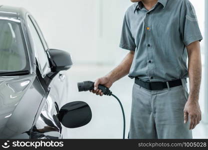 Senior asian Technician is charging the electric car or EV in service center for maintainance, Eco-friendly alternative energy concept