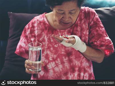 Senior asian woman take pill medicine on hand while sitting on sofa at home