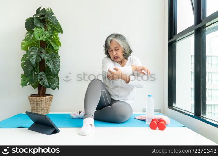 Senior Asian woman watχng onli≠courses on a laptop whi≤exercising in the living room at home. Concept of workout training onli≠.
