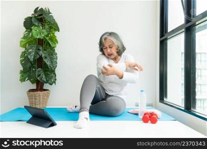 Senior Asian woman watχng onli≠courses on a laptop whi≤exercising in the living room at home. Concept of workout training onli≠.