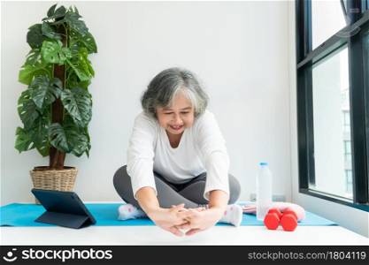 Senior Asian woman watching online courses on a laptop while exercising in the living room at home. Concept of workout training online.