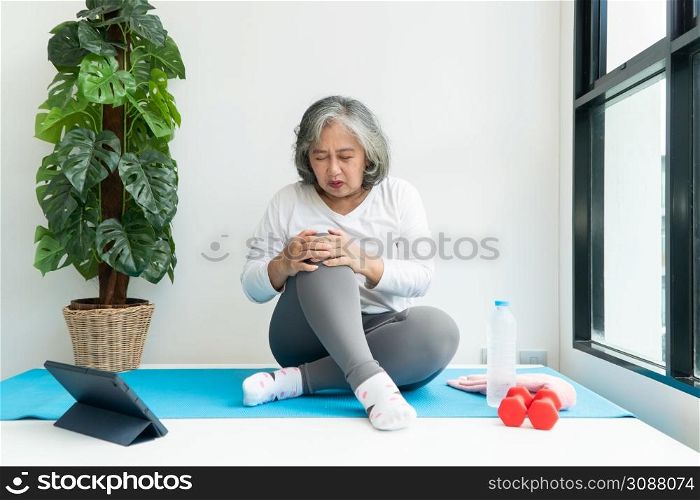 Senior Asian woman watching online courses on a laptop while exercising in the living room at home. Concept of workout training online.