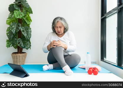 Senior Asian woman watching online courses on a laptop while exercising in the living room at home. Concept of workout training online.