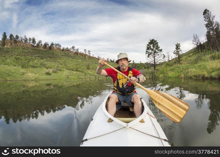 senior athletic paddler in a decked expedition canoe on a lake with green vegetation - Horsetooth Reservoir, Fort Collins, Colorado