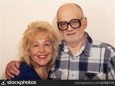 Senior bearded man in glasses hugs smiling senior woman over beige background