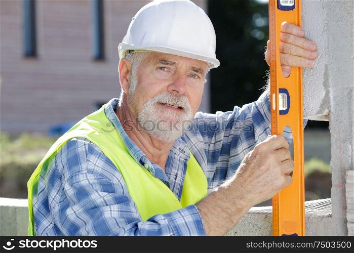 senior builder holding angled spirit level to wall