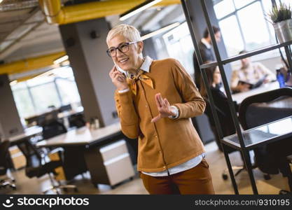 Senior busi≠sswoman using mobi≤pho≠at office whi≤other peop≤having meeting in background