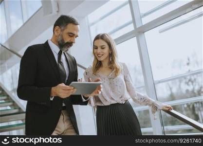 Senior business man and his pretty young female colleague standing in office with digital tablet