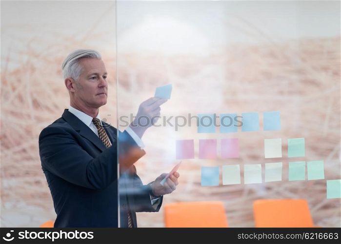 senior business man at modern office making plans and projects with post stickers on glass