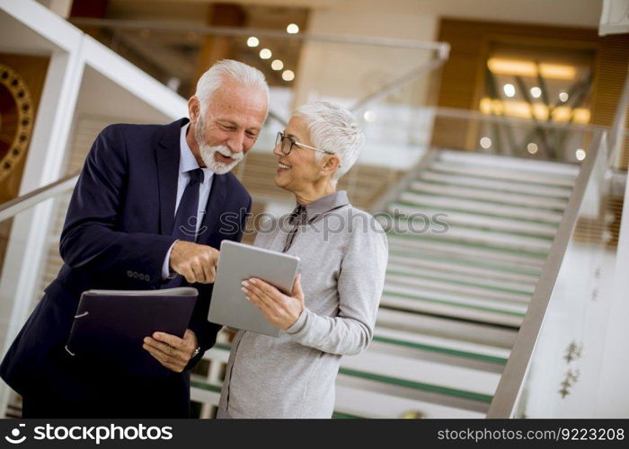 Senior business people standing in office with tablet and paper documents