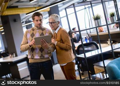 Senior business woman and her young colleague standing in the office with digital tablet