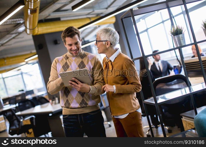 Senior business woman and her young colleague standing in the office with digital tablet