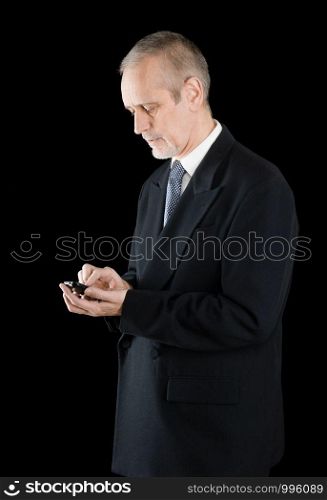 Senior businessman in black suit writing sms or dialing a number on his mobile phone, on black background