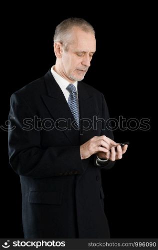 Senior businessman in black suit writing sms or dialing a number on his mobile phone, on black background
