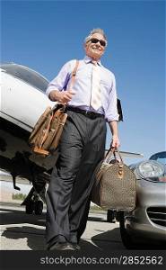Senior businessman in front of car and airplane, low angle view.