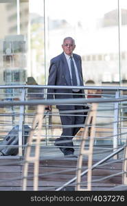 Senior businessman leaving hotel with wheeled suitcase