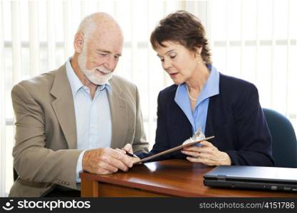 Senior businessman signs a contract with the assistance of a mature businesswoman.