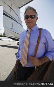 Senior businessman standing in front of private airplane.