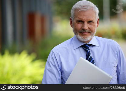 Senior businessman stood outdoors with laptop