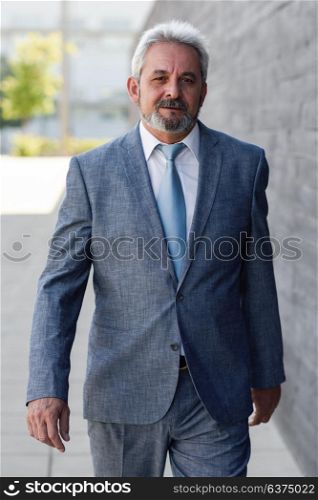 Senior businessman walking outside of modern office building. Successful business man wearing formal suit and tie in urban background.