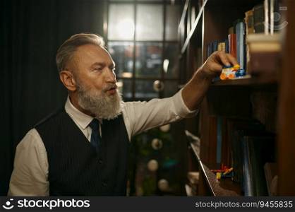 Senior businessman with old-fashioned outfit playing toy train on bookshelf in home or office library. Senior businessman with old-fashioned outfit playing toys in library