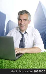 senior businessman working green grass desk computer city modern buildings