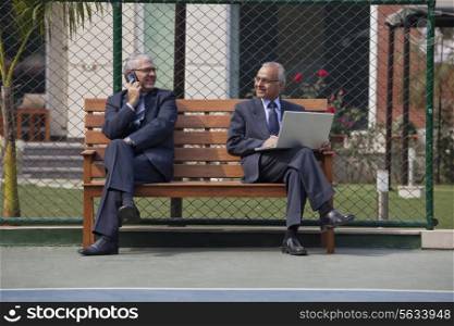 Senior businessmen looking at each other while using cell phone and laptop