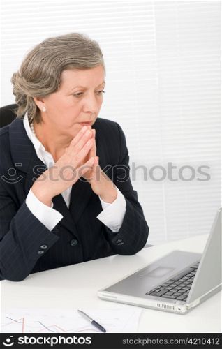 Senior businesswoman looking seriously at computer sitting behind office table
