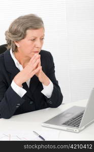 Senior businesswoman looking seriously at computer sitting behind office table