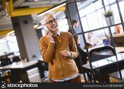 Senior businesswoman using mobile phone at office while other people having meeting in background