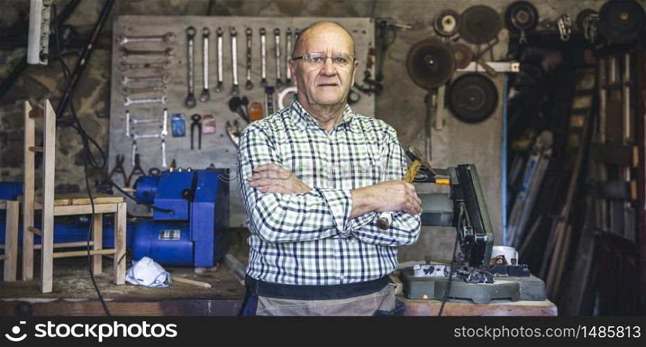 Senior carpenter posing with crossed arms in his workshop. Carpenter in his workshop