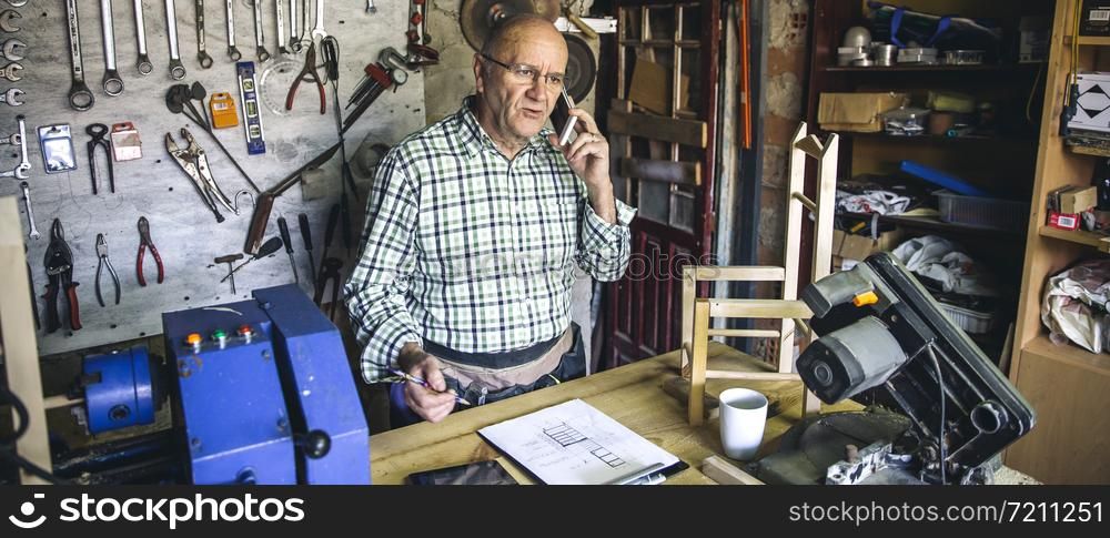 Senior carpenter talking on the phone in his workshop. Carpenter in his workshop