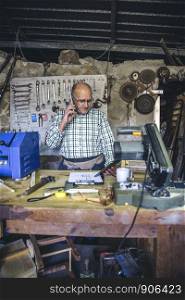 Senior carpenter talking on the phone in his workshop. Carpenter in his workshop