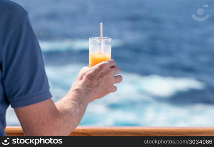 Senior caucasian adult man with tequila sunrise. Senior caucasian adult man with tequila sunrise in glass on teak balcony rail of ocean cruise ship. Senior caucasian adult man with tequila sunrise