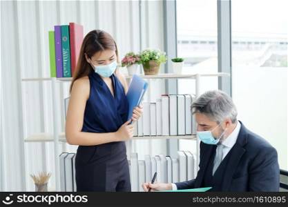 Senior Caucasian boss and young businesswoman wearing mask preventing for Covid 19 virus holding document sheet and talking about job in office. Social distance and new normal lifestyle concept