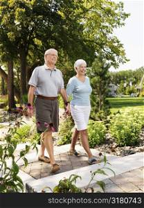 Senior Caucasian couple holding hands and walking outdoors in park.
