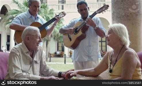 Senior caucasian couple sitting in bar at hotel and listening to musicians playing guitar