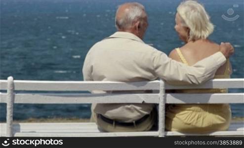 Senior caucasian couple sitting on bench near the sea and hugging