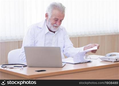 Senior caucasian doctor sitting on working desk with laptop and stethoscope. Hospital and Health Concept.