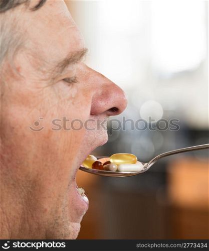 Senior caucasian male eating a spoonful of vitamin tablets for breakfast in kitchen
