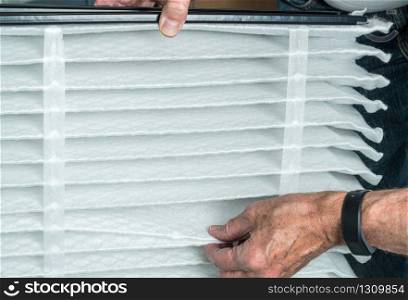 Senior caucasian man checking a clean folded air filter in the HVAC furnace system in basement of home. Senior man inserting a new air filter in a HVAC Furnace