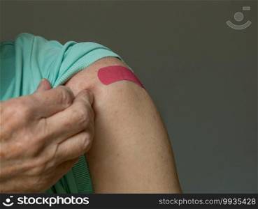 Senior caucasian man holding up shirt sleeve to show the bandaid after coronavirus vaccine shot in the shoulder. Senior man holding up shirt after covid-19 vaccine injection